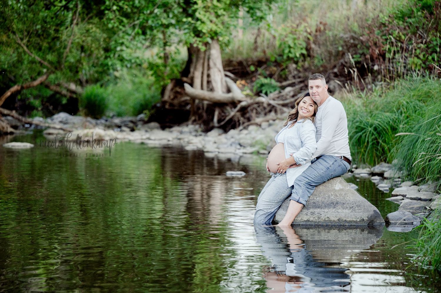 Couple sitting intimately by a serene stream surrounded by greenery.