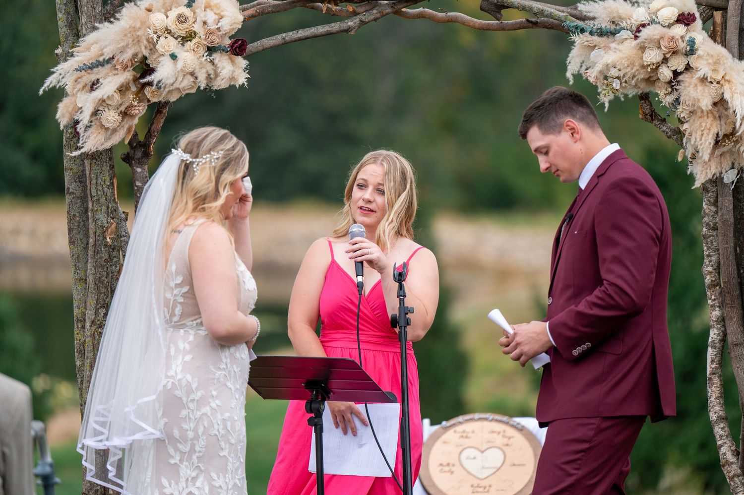 Wedding ceremony with bright pink-dressed officiant under rustic floral arch.