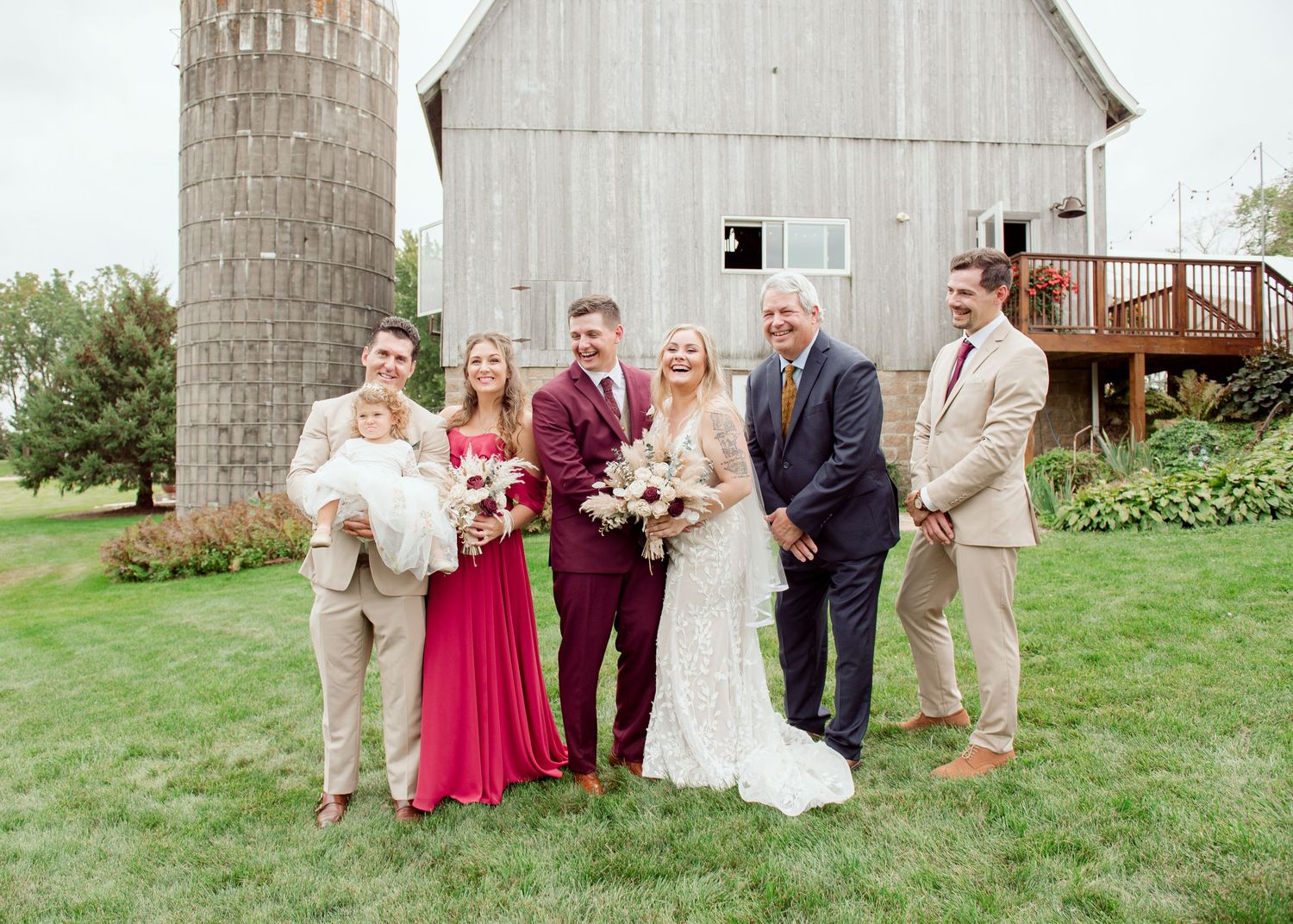 Wedding party poses for formal group photo in front of white barn with silo.