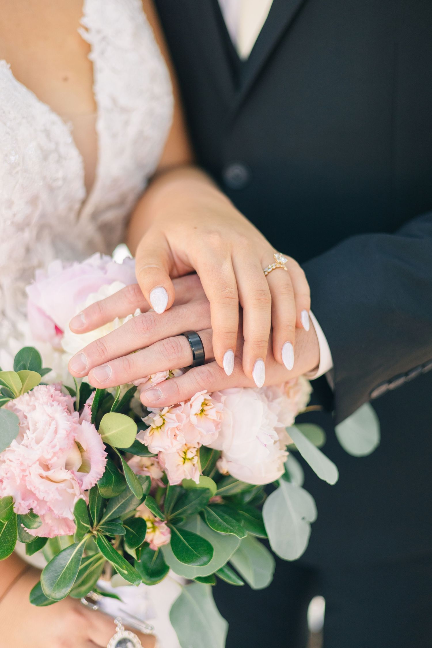 Bride and groom showing wedding rings resting on pink peony bouquet.