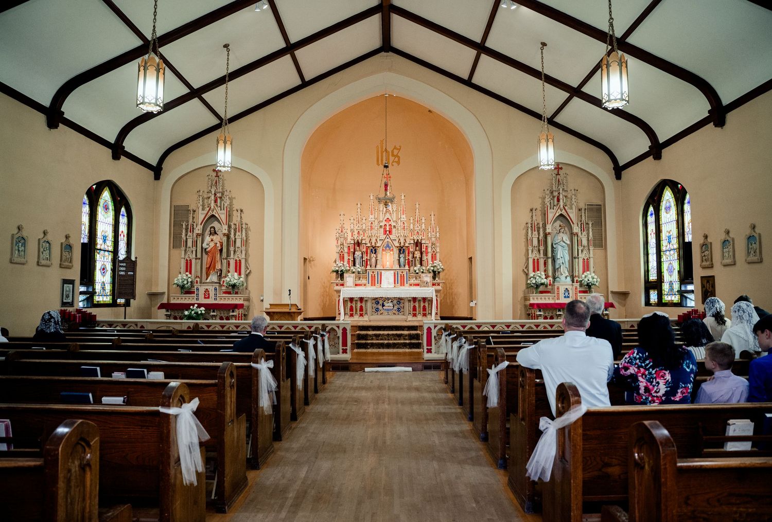 Interior view of a traditional church sanctuary with wooden pews and vaulted ceiling illuminated by pendant lights.