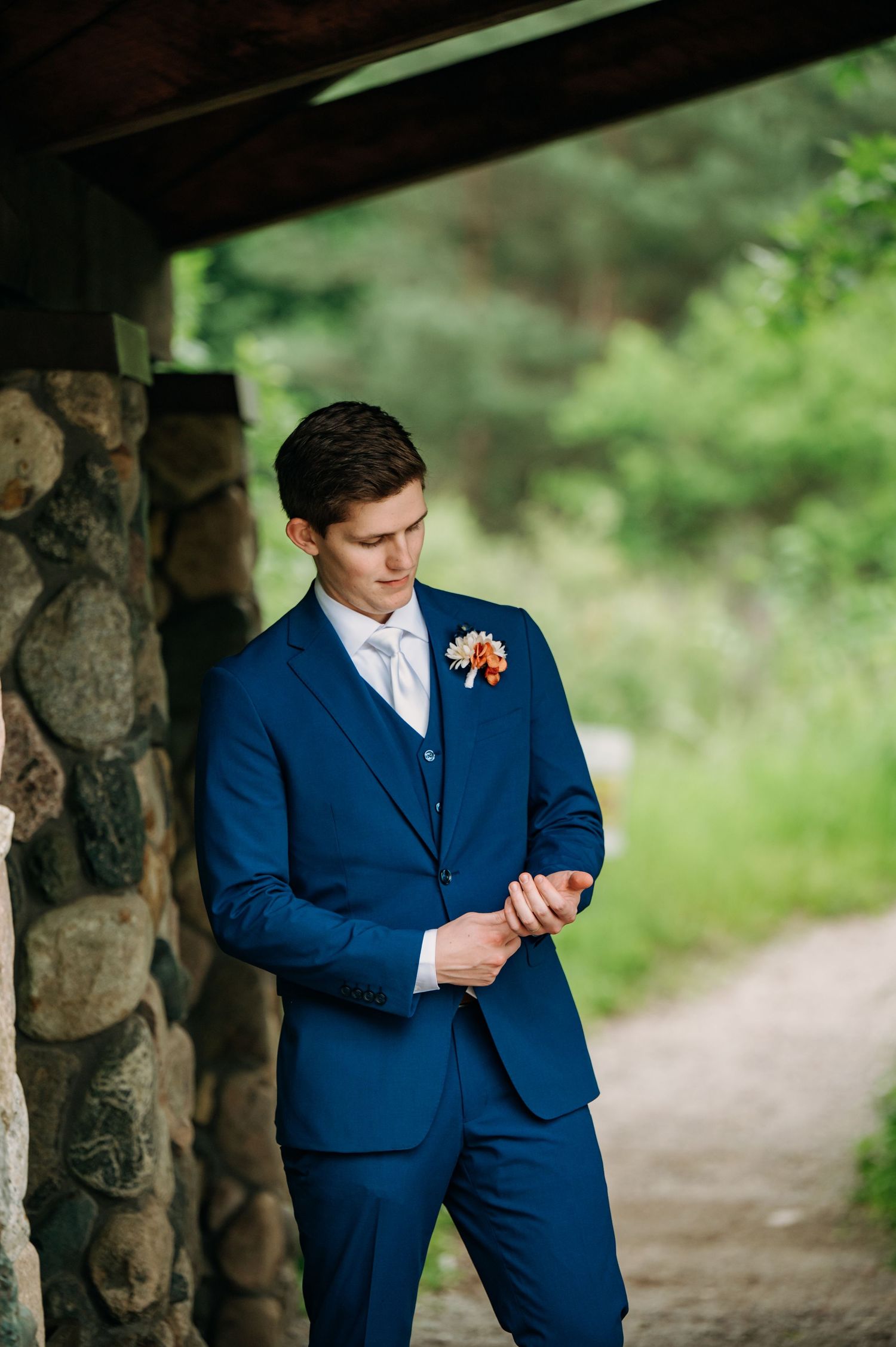 A person in a navy blue suit checks their phone while standing in a rustic stone archway outdoors.