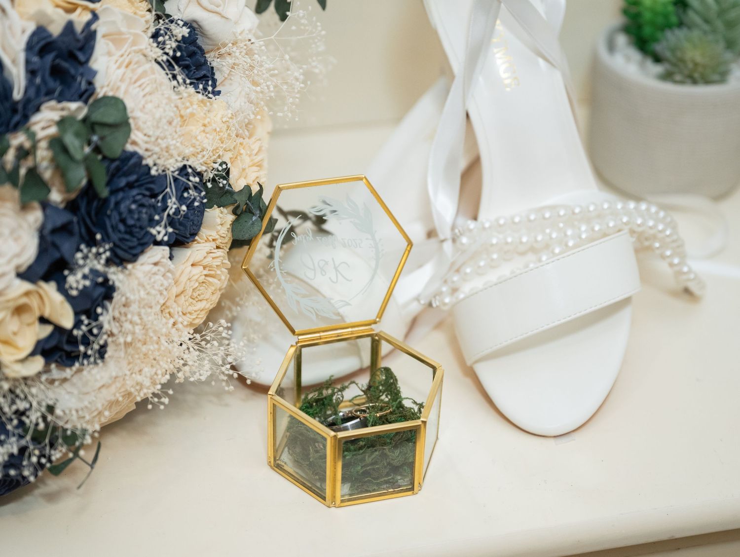 Gold geometric glass jewelry box with black dried flowers on white marble surface for wedding decor styling.