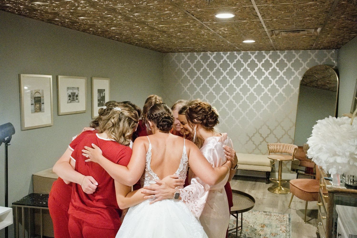 Bridesmaids and bride share emotional group hug in bridal suite before wedding ceremony.