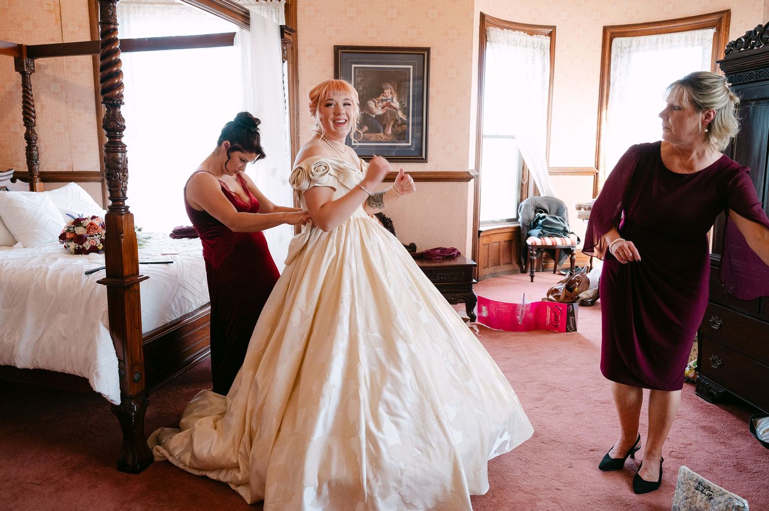 Central MN Wedding Photos | Smiling bride in gold ball gown gets final adjustments from bridesmaids before wedding ceremony.