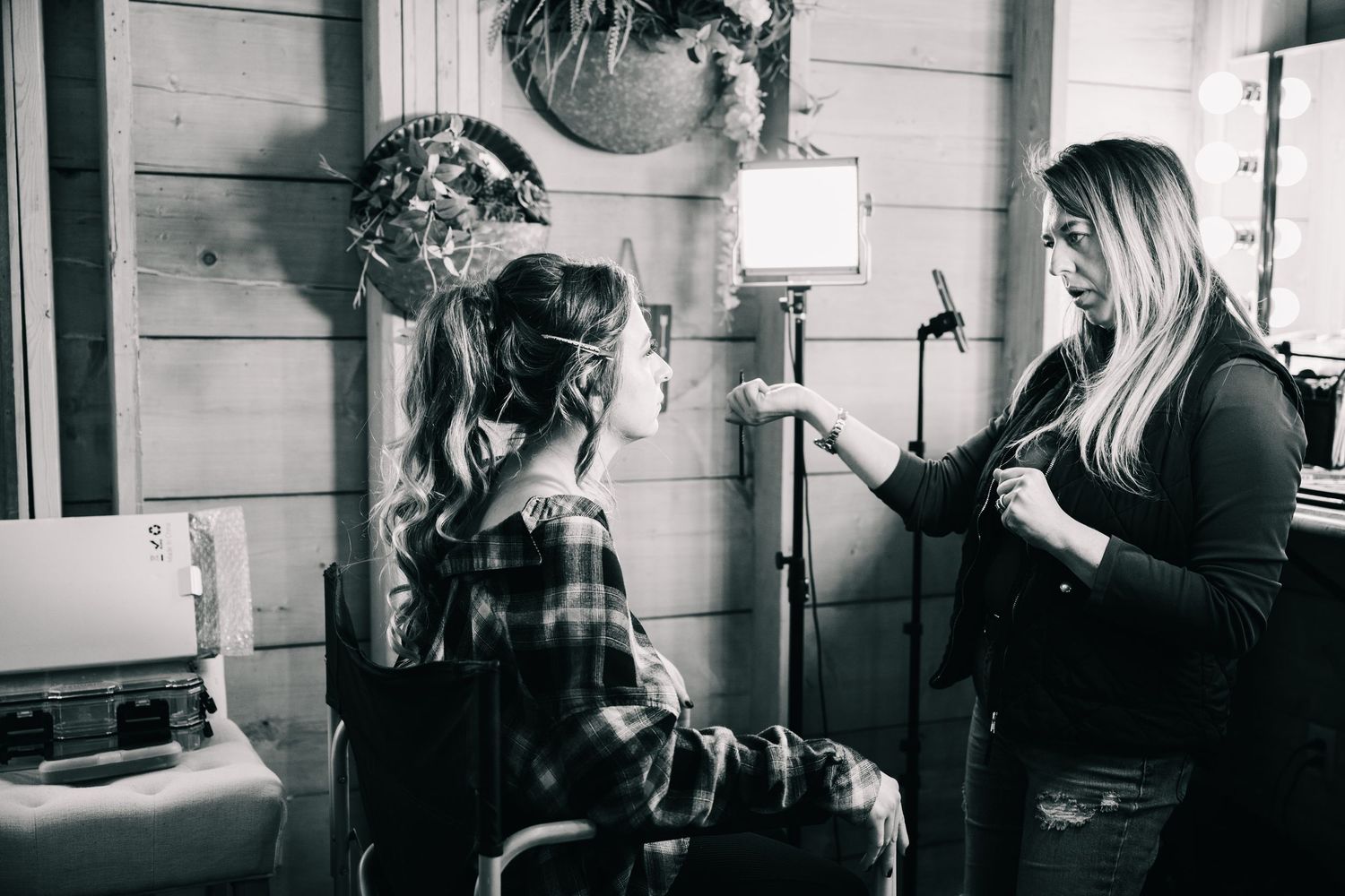Black and white photo of a woman getting hair styled by a professional stylist under bright studio lighting.
