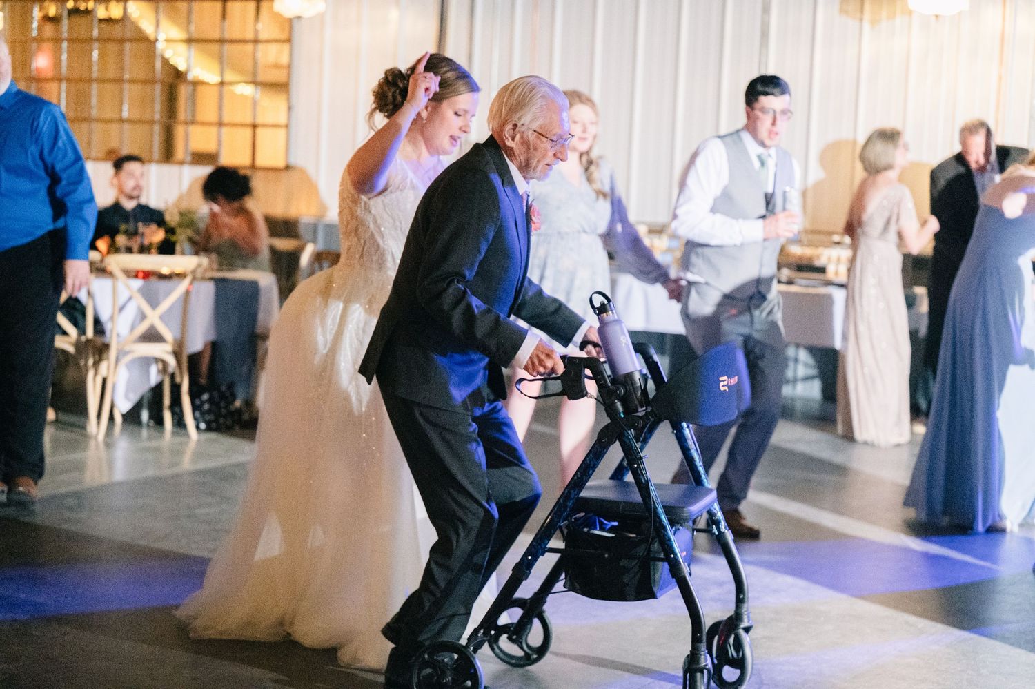 Bride dancing with elderly guest using a walker during a heartwarming wedding reception on the dance floor.