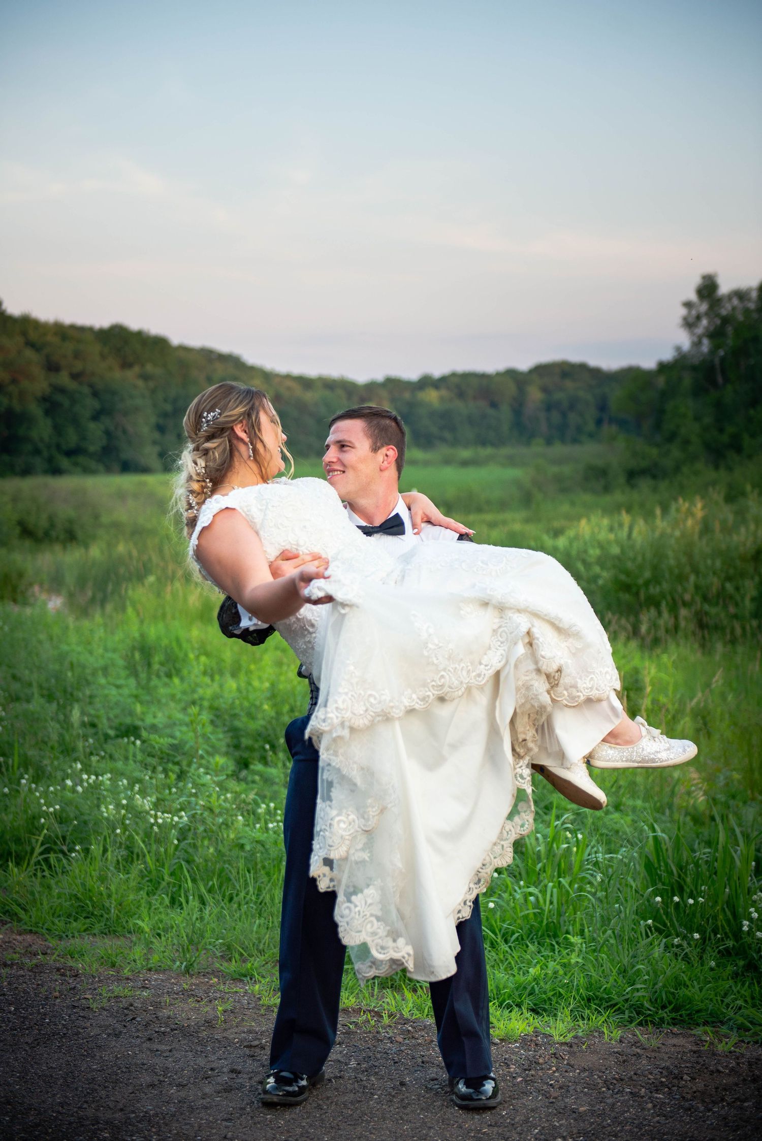Groom carries bride in traditional pose against a sunset meadow backdrop.  Zimmerman MN Weddings