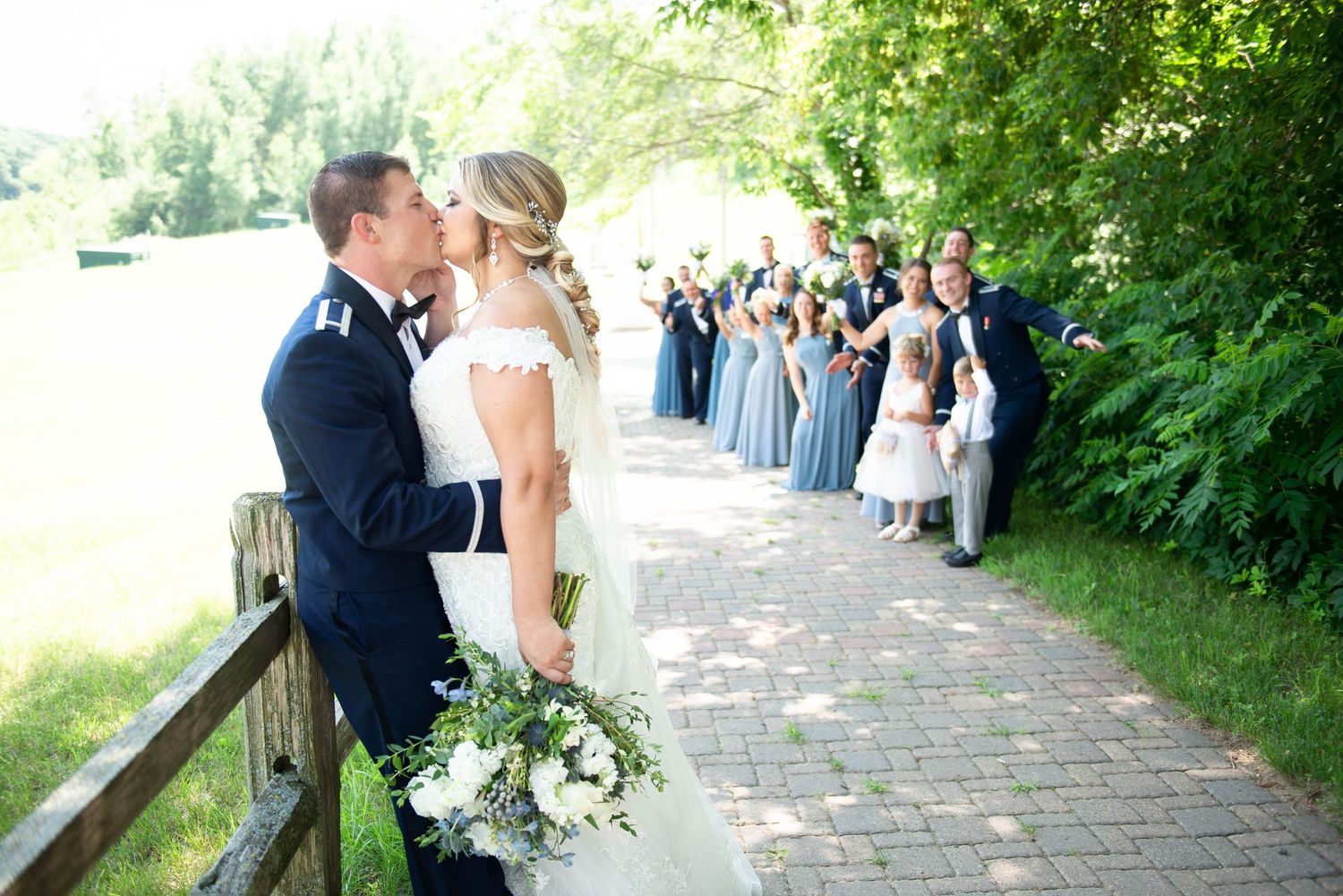 Wedding party walking along a charming brick pathway surrounded by lush greenery on a sunny day. Zimmerman MN Weddings