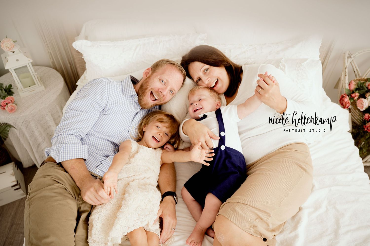 Family lifestyle portrait of parents and children cuddling together on white bed.