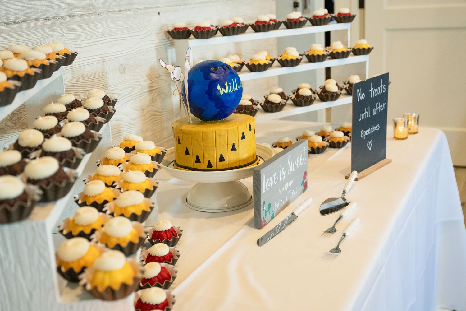 Elegant wedding dessert table featuring cupcakes, a small cake, and tiered white stands at a reception.