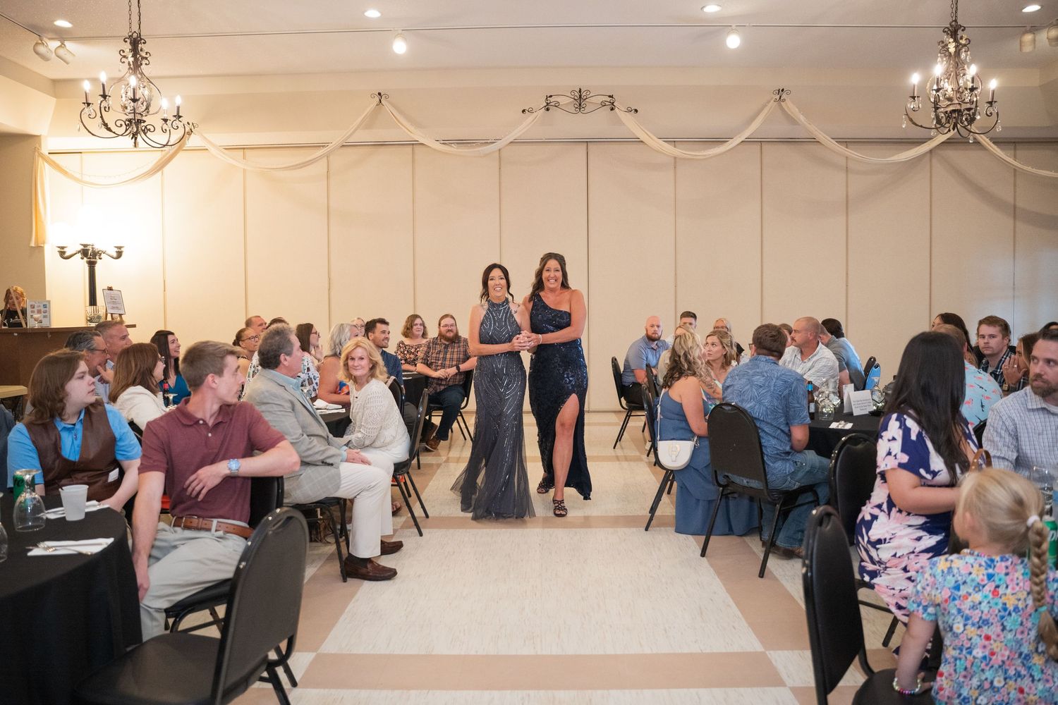 Wedding reception guests seated at round tables in an elegant banquet hall with chandeliers. Pease Minnesota Wedding at Northern Lights Ball