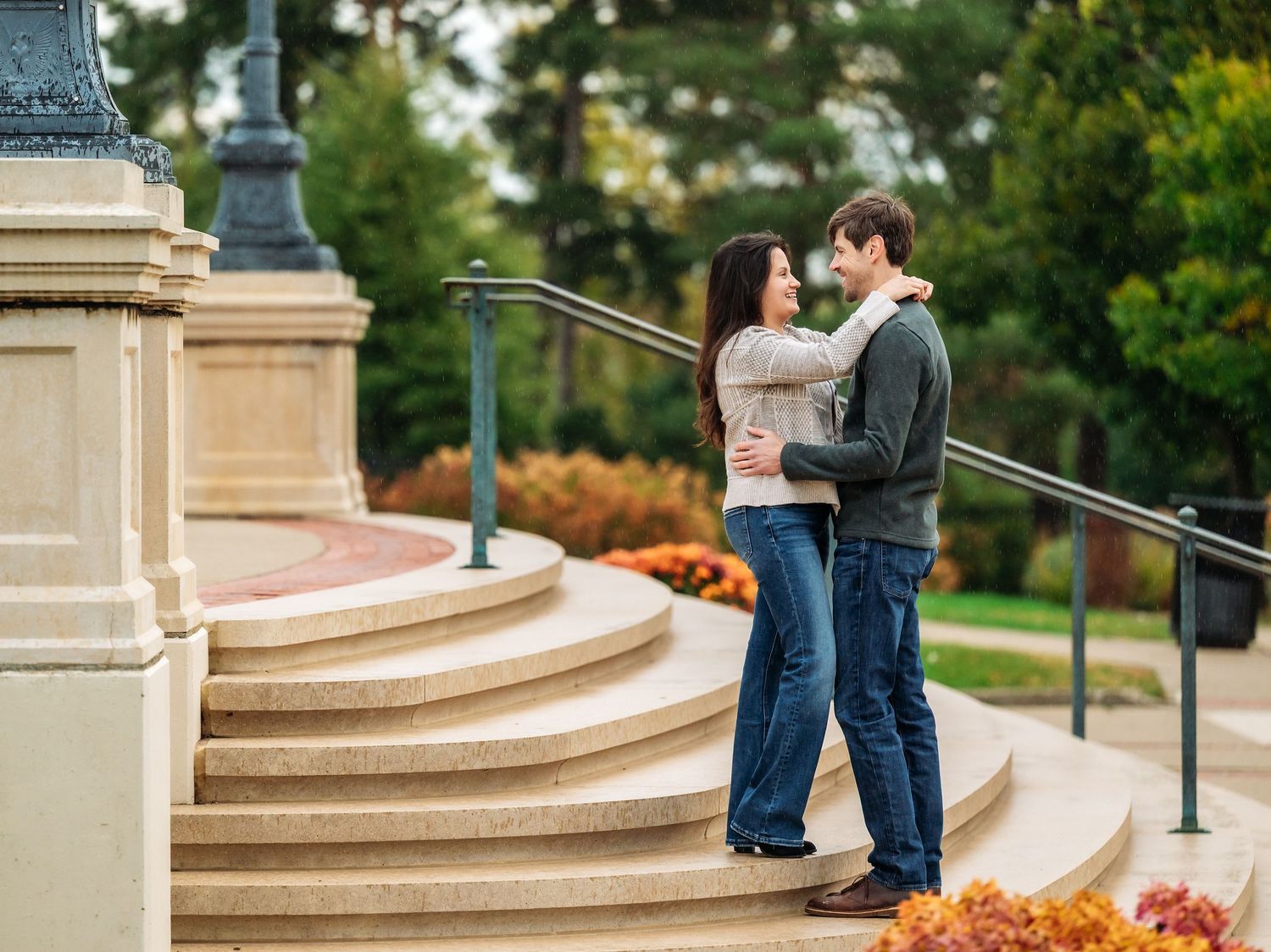 A couple stands on stone steps in a park setting during a romantic outdoor engagement photo session at Lake Como. Engagement Sessions Minne.