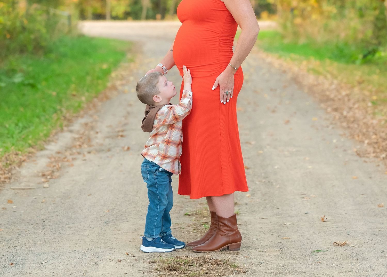 A person in a bright orange dress walks with a small child along a scenic autumn path through the woods.