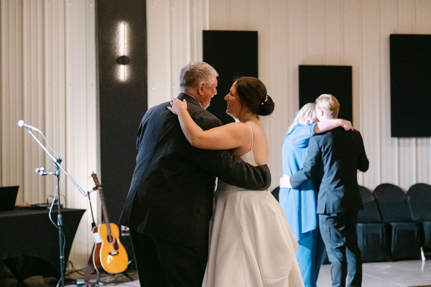 Wedding reception dance floor with couples dancing in an elegant white-walled venue.