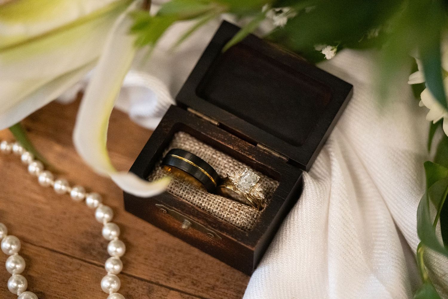 Wedding accessories including rings, pearls and delicate decor items arranged on a wooden surface.
