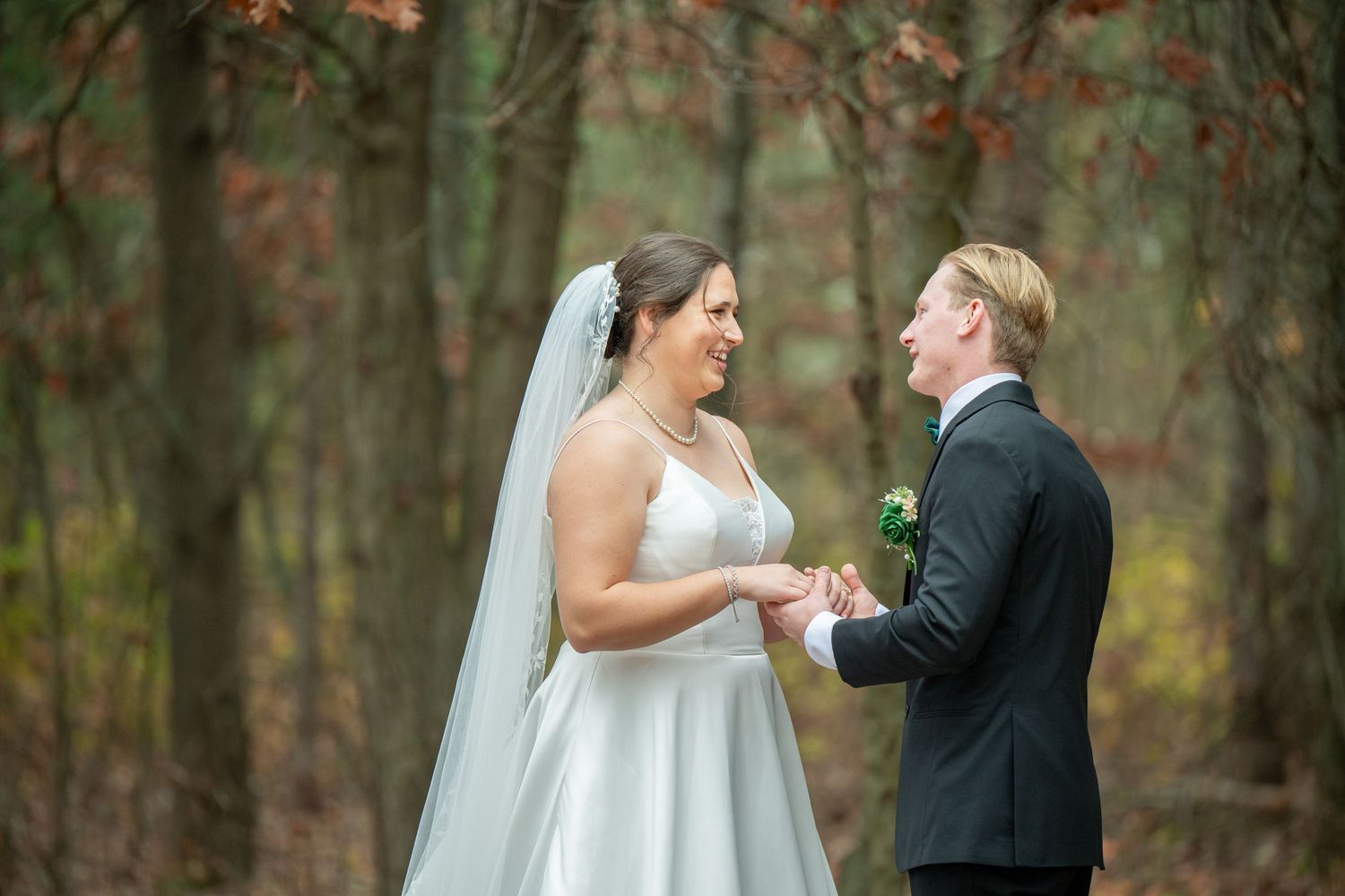 Newlyweds exchange loving glances while standing among trees with autumn foliage in the background.