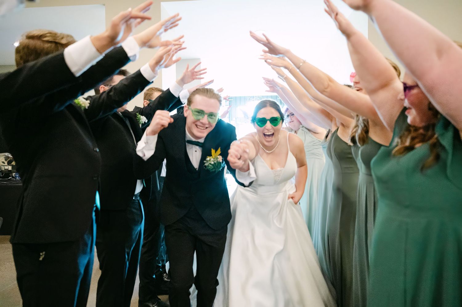 Wedding party creates archway tunnel with raised arms for newlyweds to walk through during celebration.