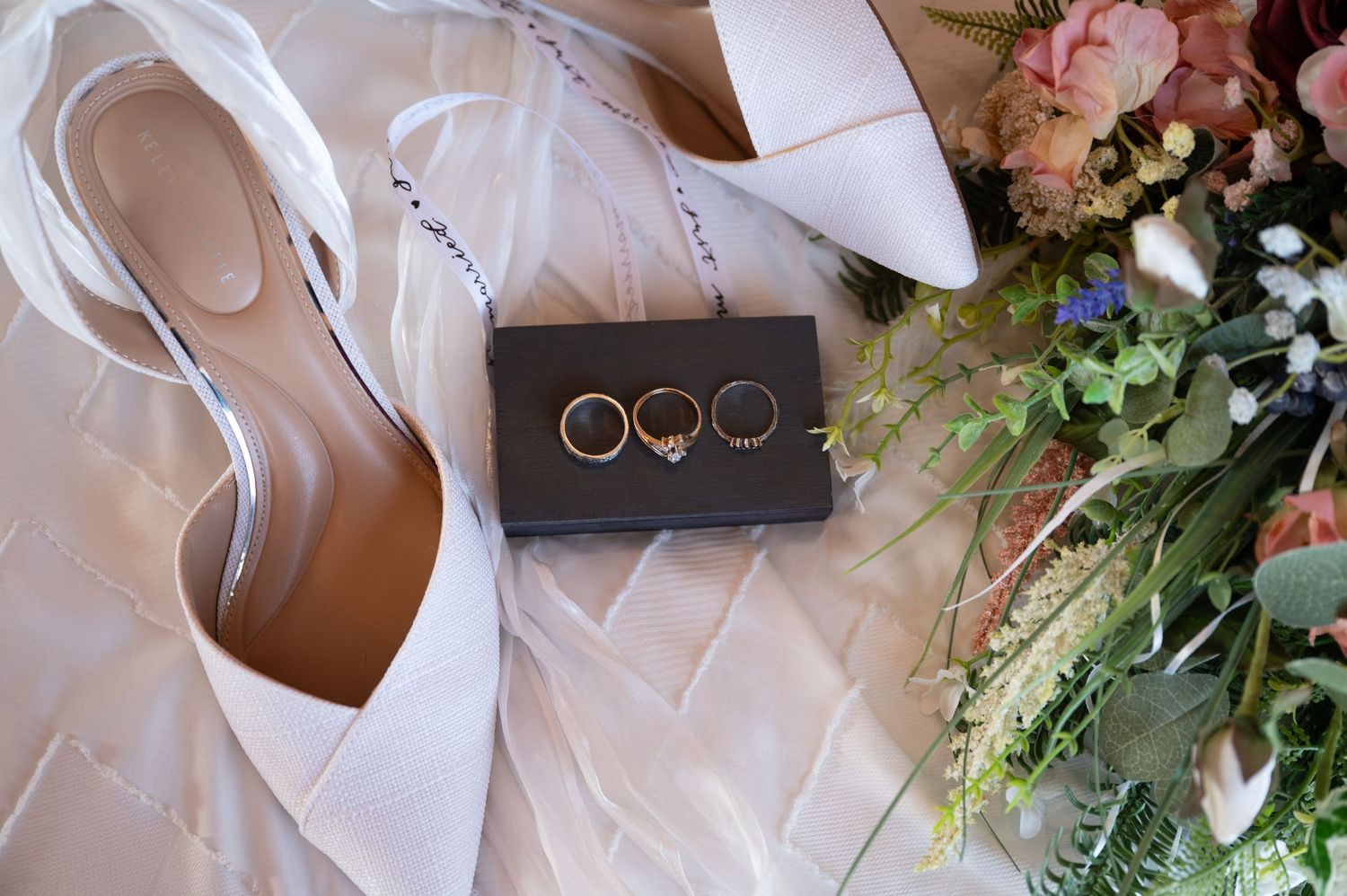 The Historic Concord Exchange Minneapolis MN. Wedding rings displayed on a dark box beside blush bridal heels and a colorful floral bouquet.