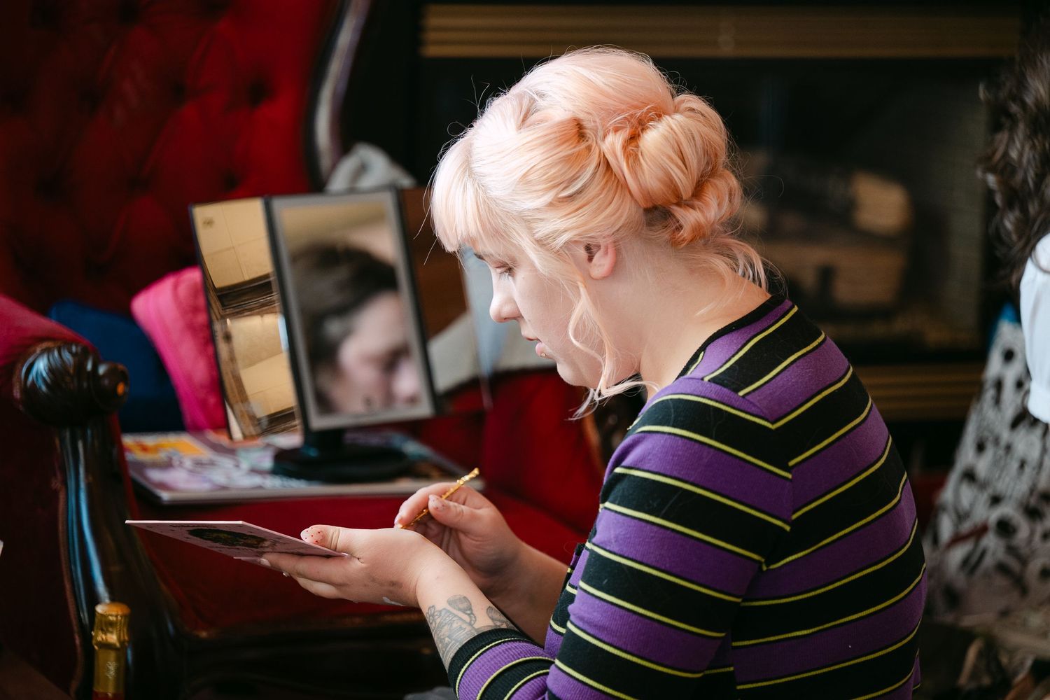 Central MN Wedding Photos | Bride with pink hair applies makeup using a mirror during wedding preparations.