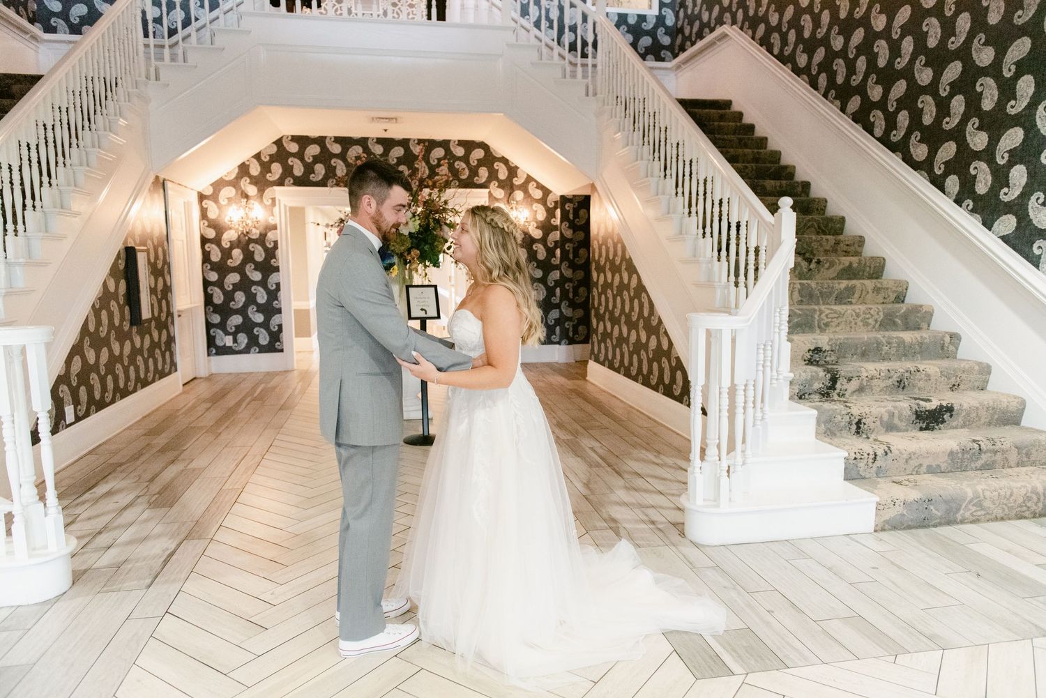 Central MN Wedding Photos | Bride and groom share first look moment at bottom of elegant double staircase.