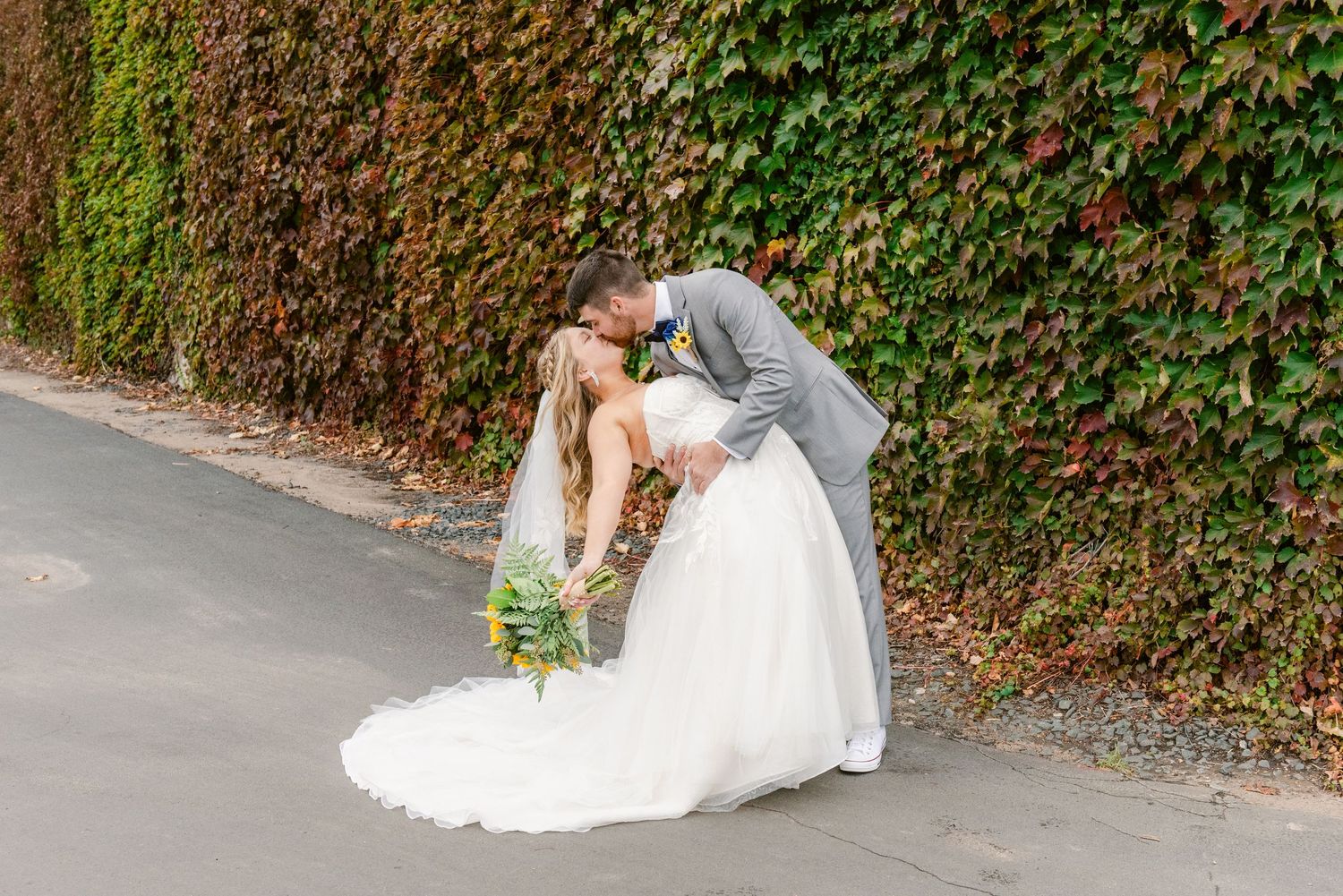 Central MN Wedding Photos | Bride and groom sharing a romantic dip kiss along ivy-covered stone wall.