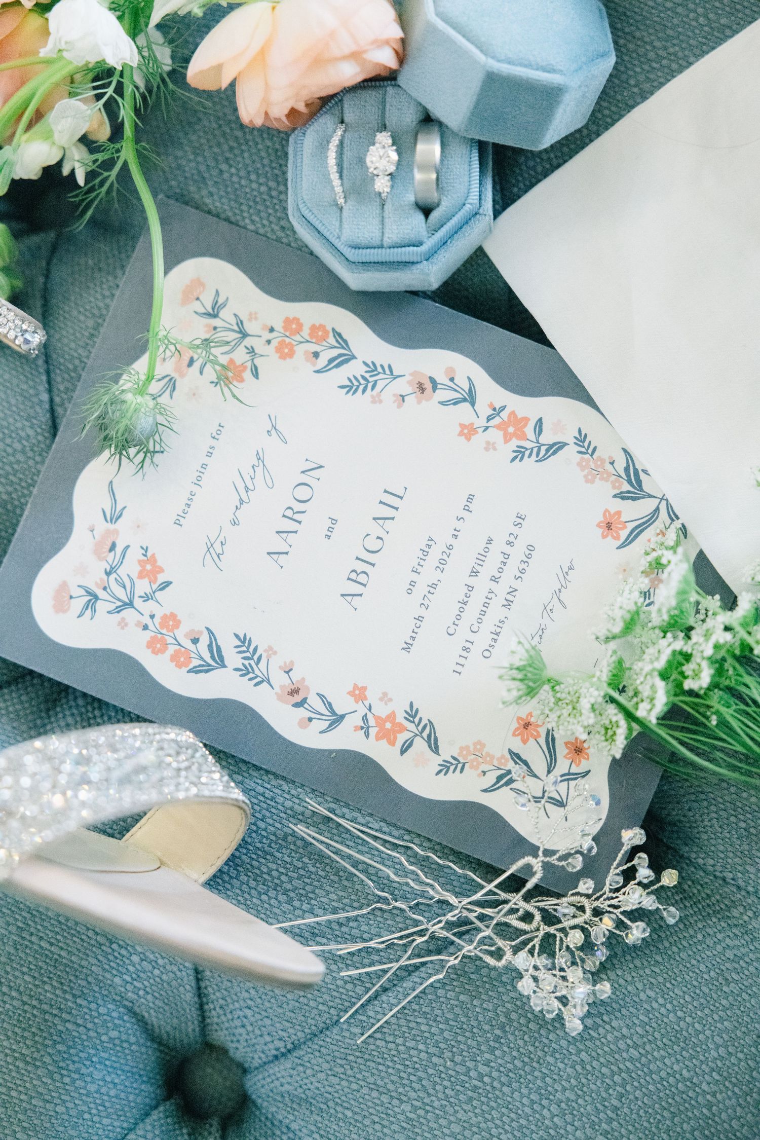 Elegant wedding invitation for Aaron and Abigail surrounded by rings, floral details, and a glittery bridal shoe.