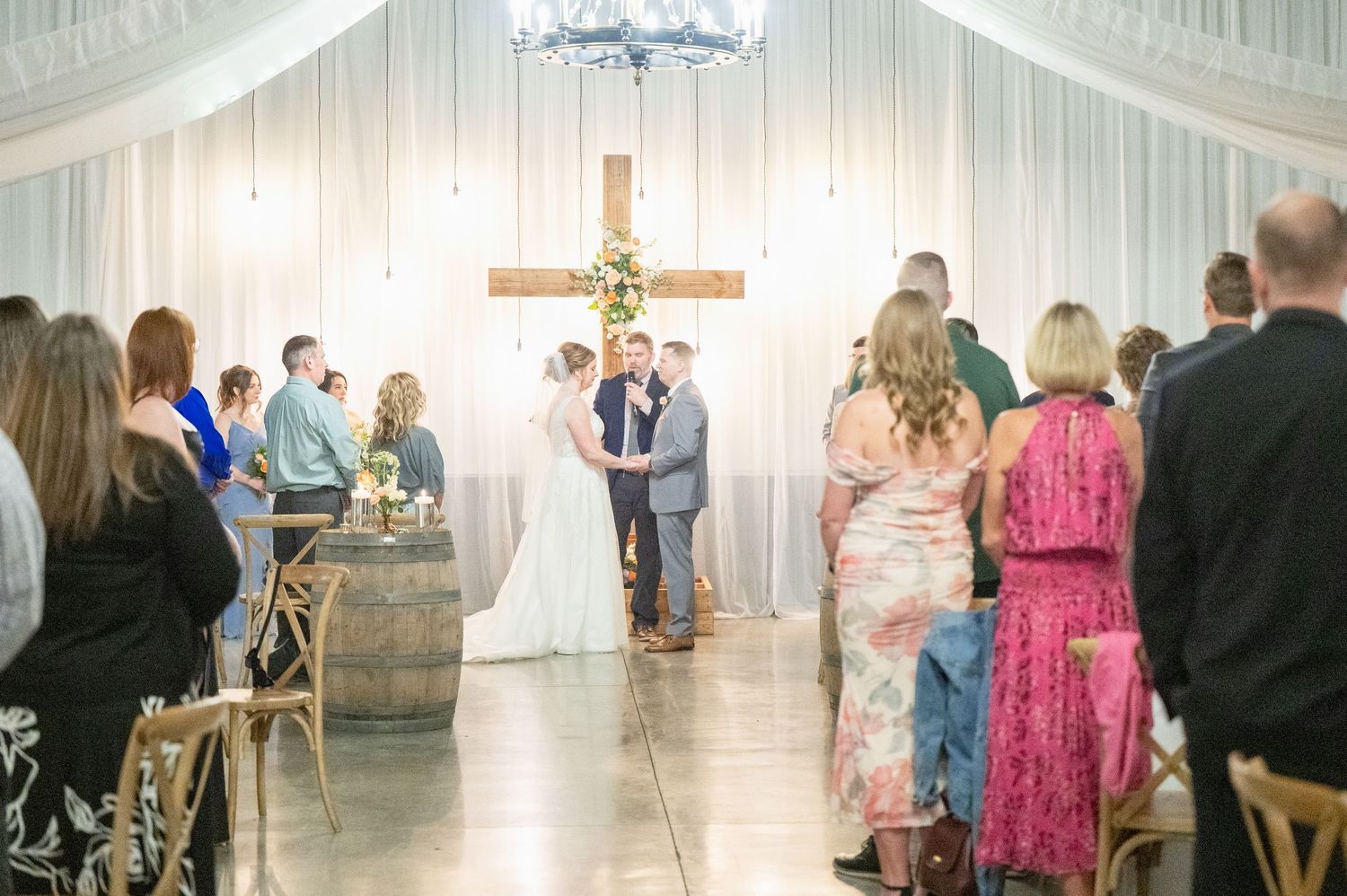 Couple exchanging vows at rustic barn wedding with wooden cross and floral decor.