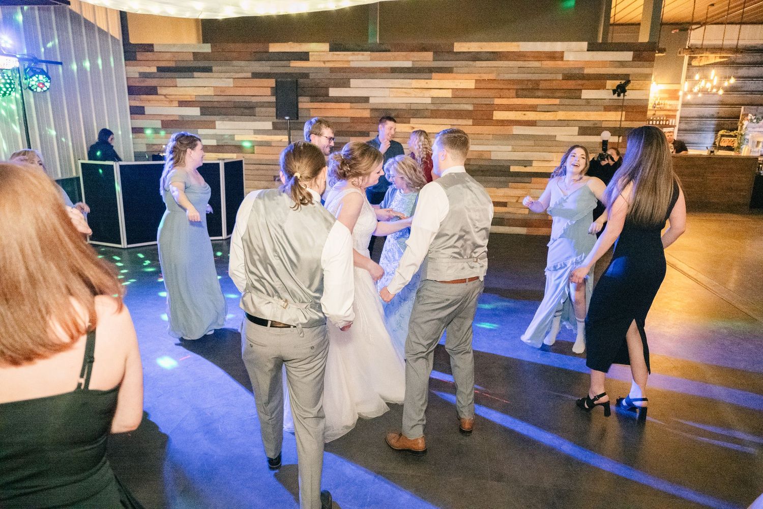 Wedding party group dance on blue-lit dance floor at reception.