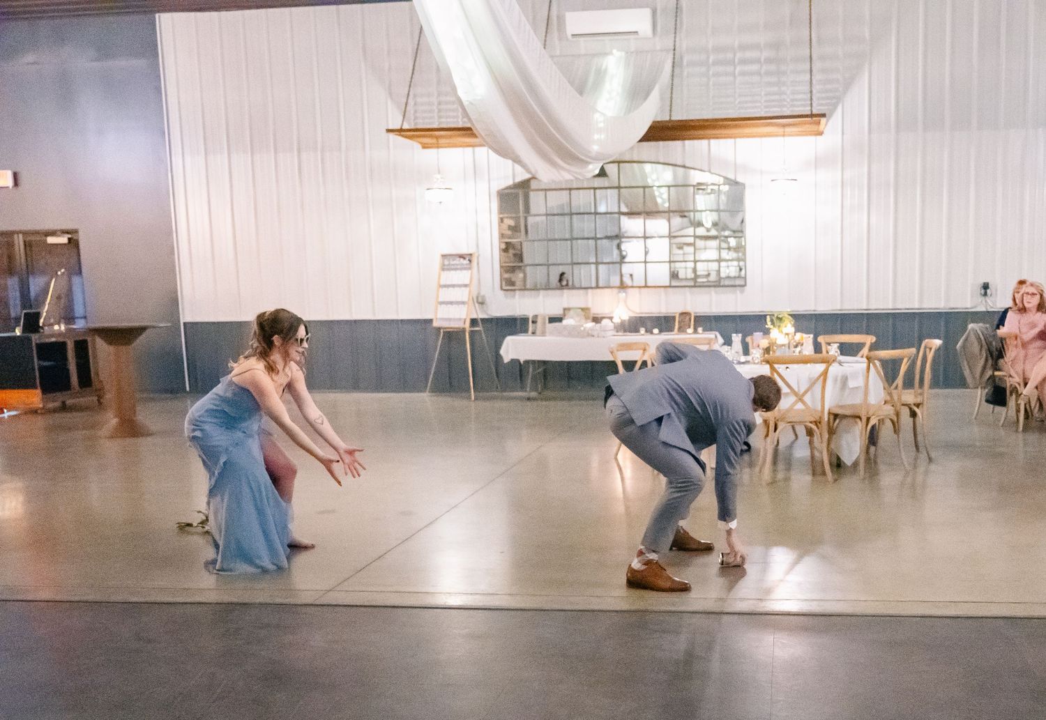 Bridesmaid and groomsman playfully facing off on dance floor at rustic wedding reception.