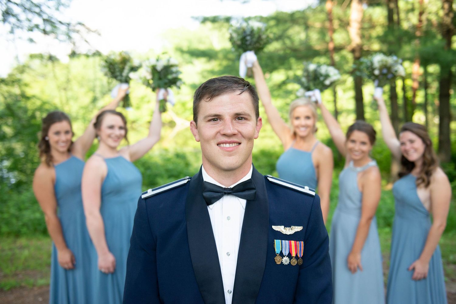 Military groom in formal attire with wedding party in light blue dresses in background. Zimmerman MN Weddings