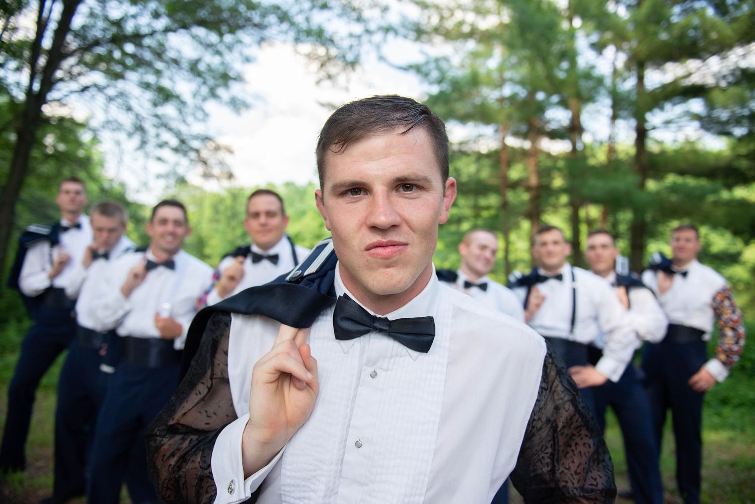 Stylish groom in bow tie with groomsmen posing playfully in the background. Zimmerman MN Weddings