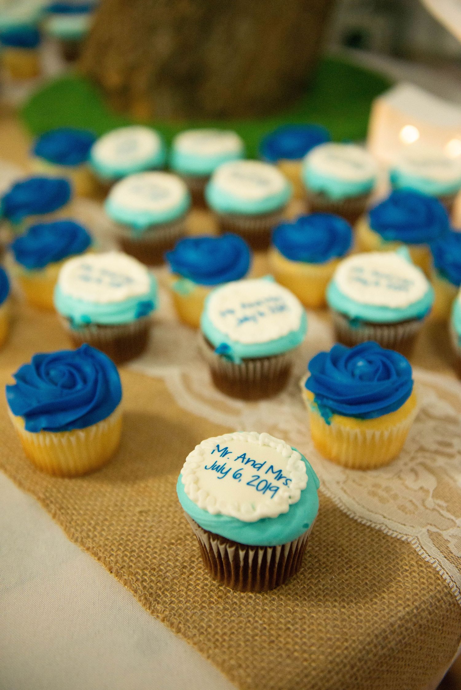Blue and turquoise frosted cupcakes arranged on a burlap surface display elegant wedding desserts. Zimmerman MN Weddings