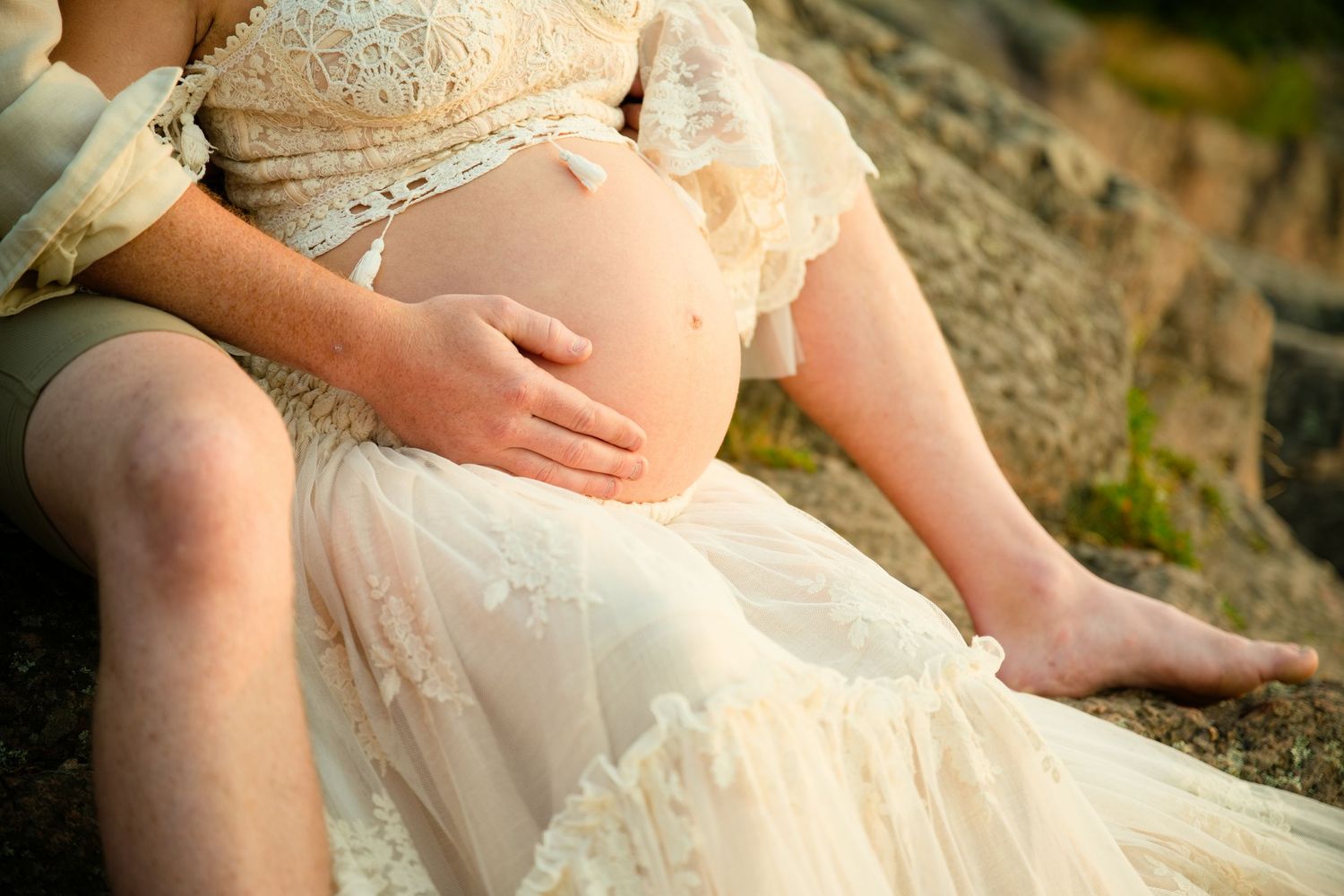 Pregnant woman in lace dress cradling baby bump outdoors during a maternity photo session.