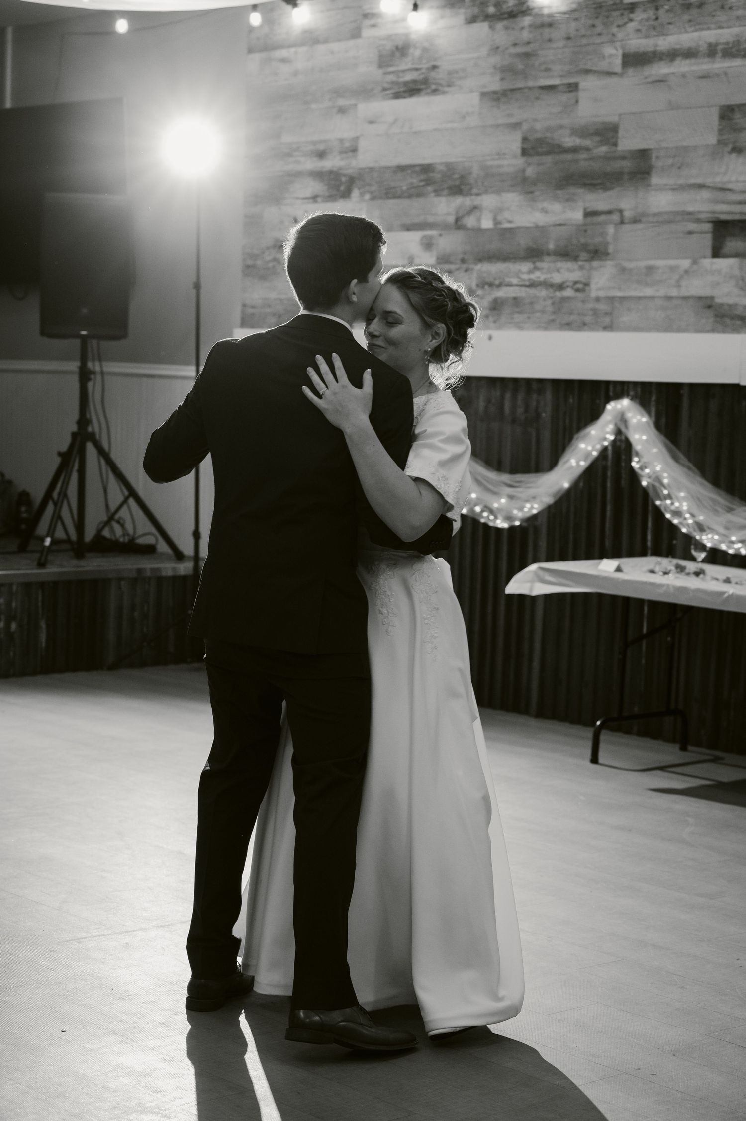 A tender moment shared during a first dance in a rustic-decorated reception venue with wooden walls.