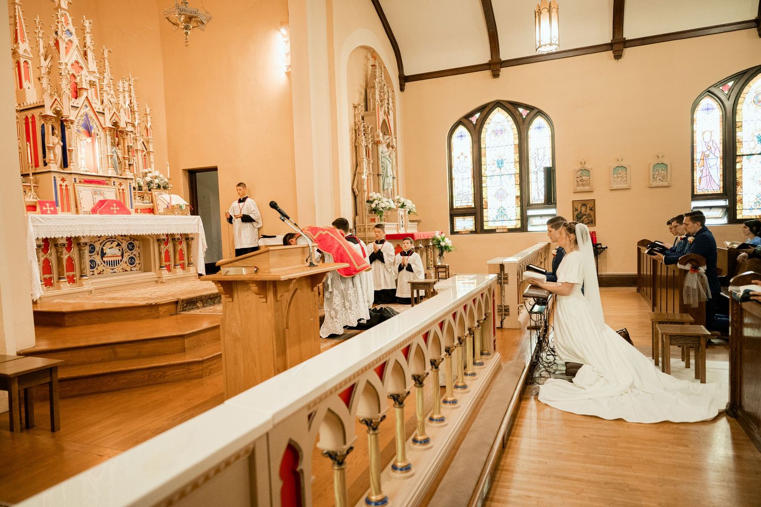 A traditional church interior with ornate wooden railings and arched windows during a wedding ceremony.