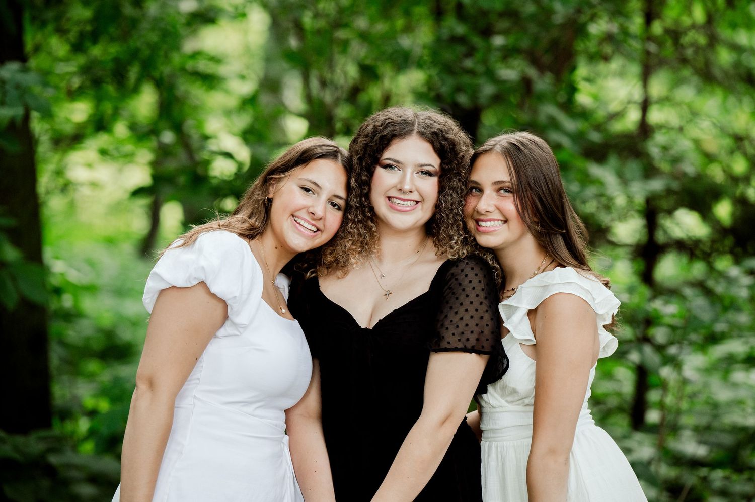 Three women smile together during outdoor portrait session in forest setting.