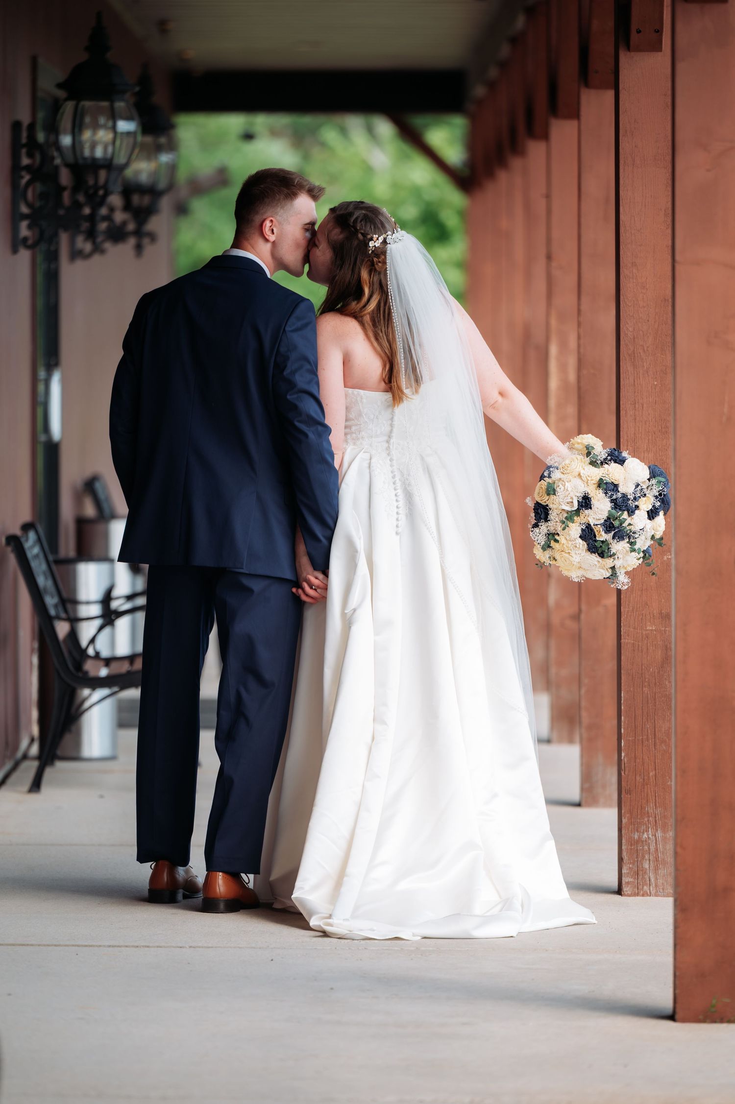 A wedding couple and ring bearer walk through a covered outdoor walkway with wooden columns. Pease Minnesota Wedding at Northern Lights Ball