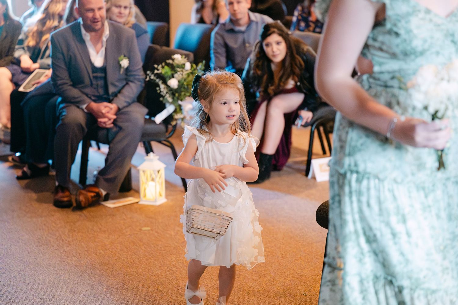 Young flower girl in white dress walks down aisle during wedding ceremony.
