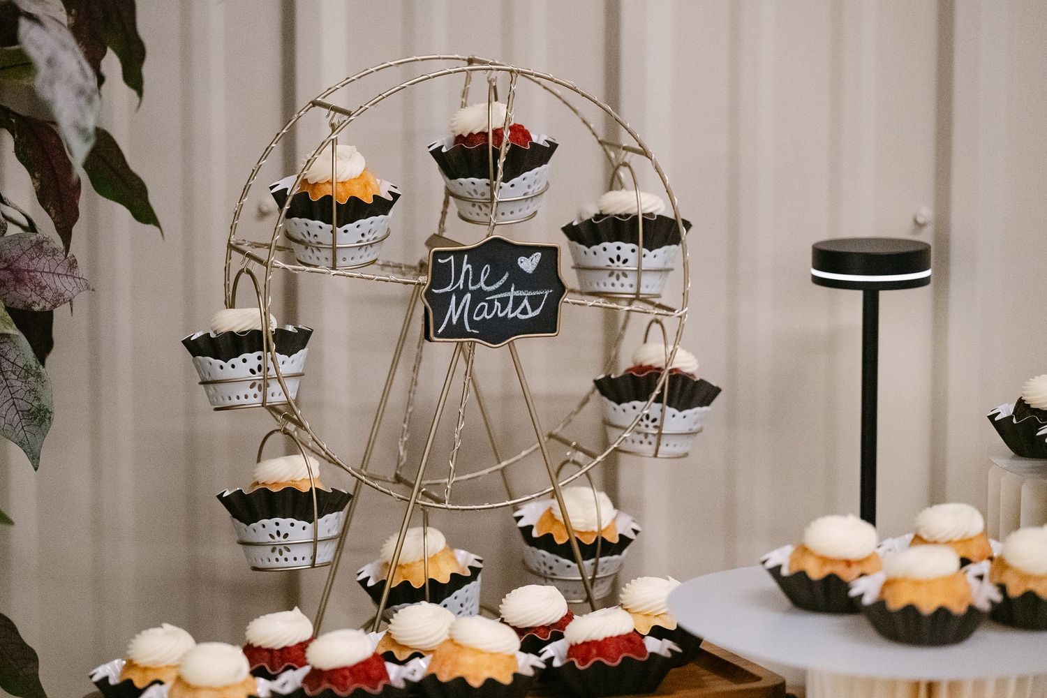 A decorative ferris wheel cupcake display stand at a wedding reception with various desserts.