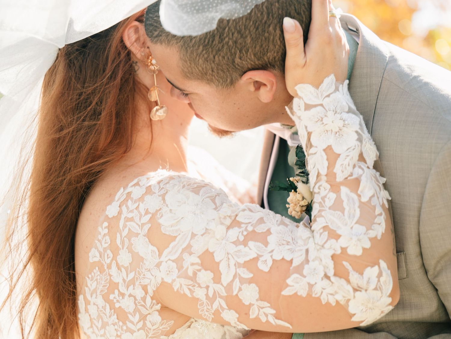 Close-up of bride in floral lace gown and groom sharing a romantic kiss beneath her veil.