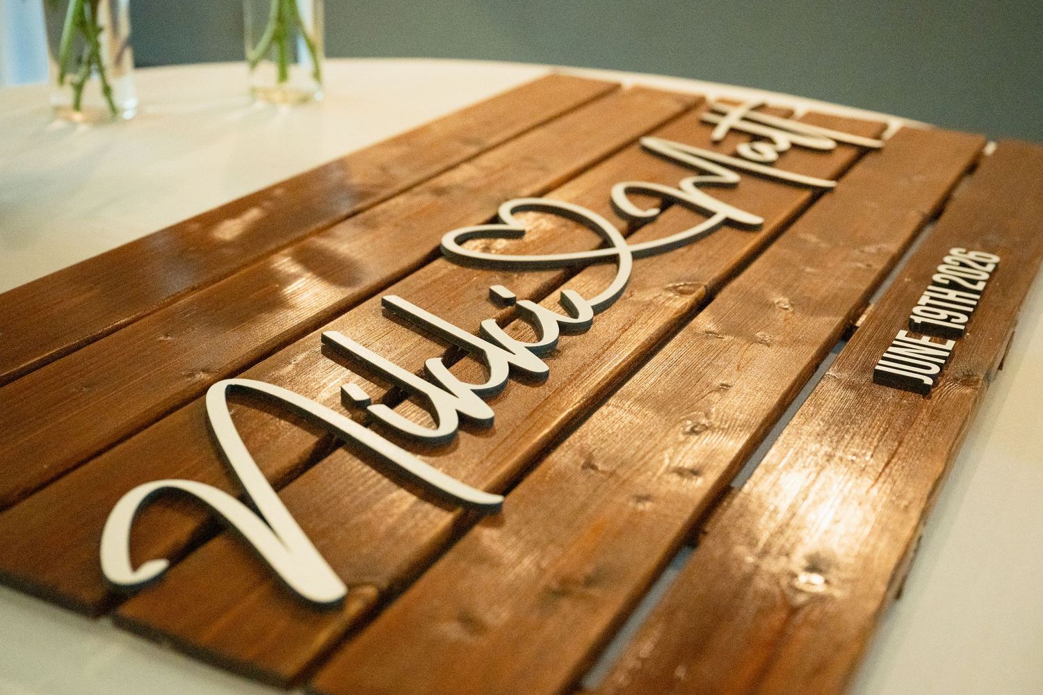 Rustic wooden wedding guest book sign with white cursive names and June date engraved on stained wood planks.