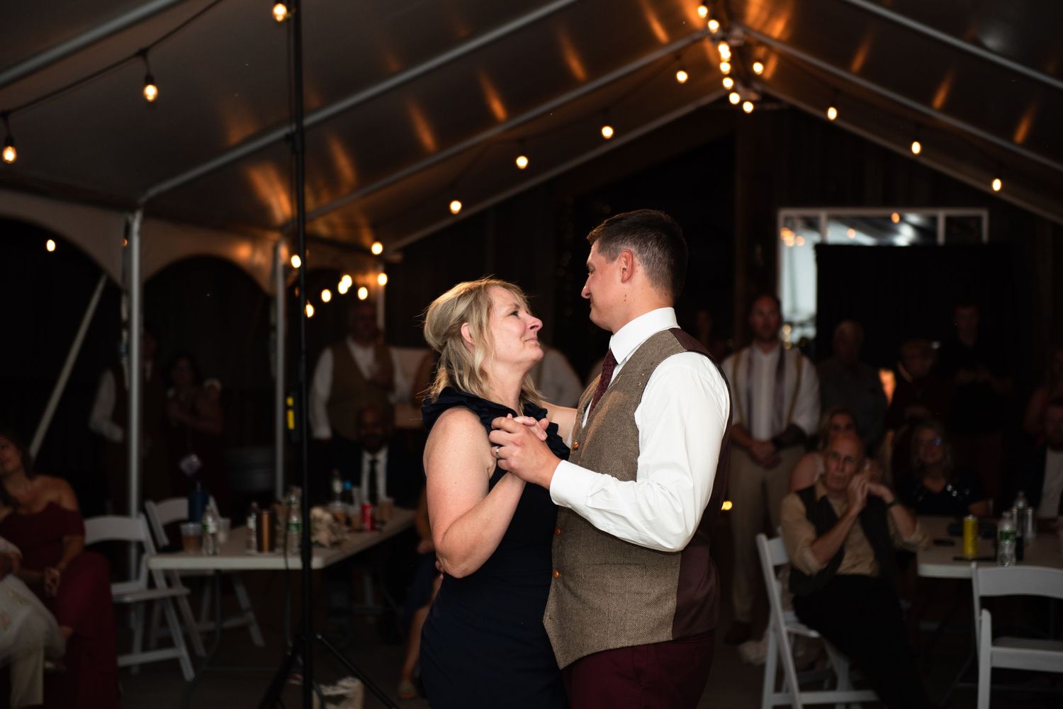 Couples dancing at an evening wedding reception under string lights in a barn venue.
