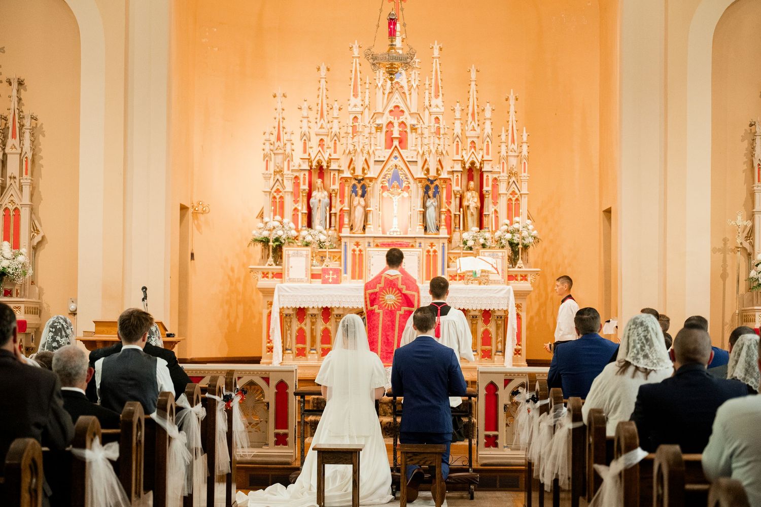Church congregation attending Mass with ornate altar and chandelier in background.