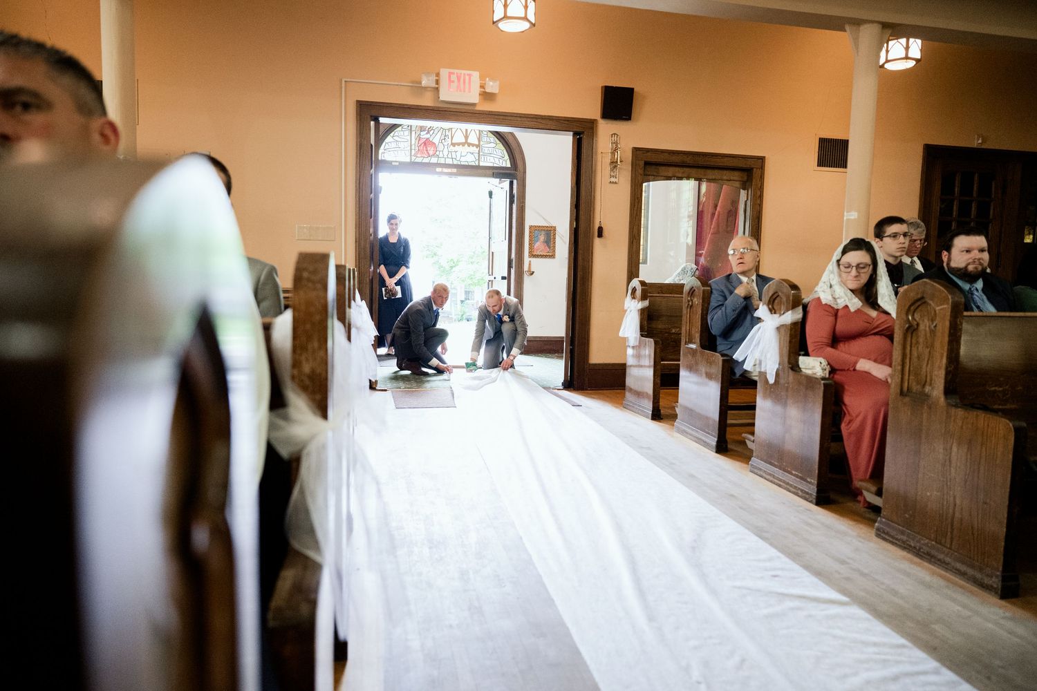 Long white aisle runner in a church with wooden pews and people seated along the sides.