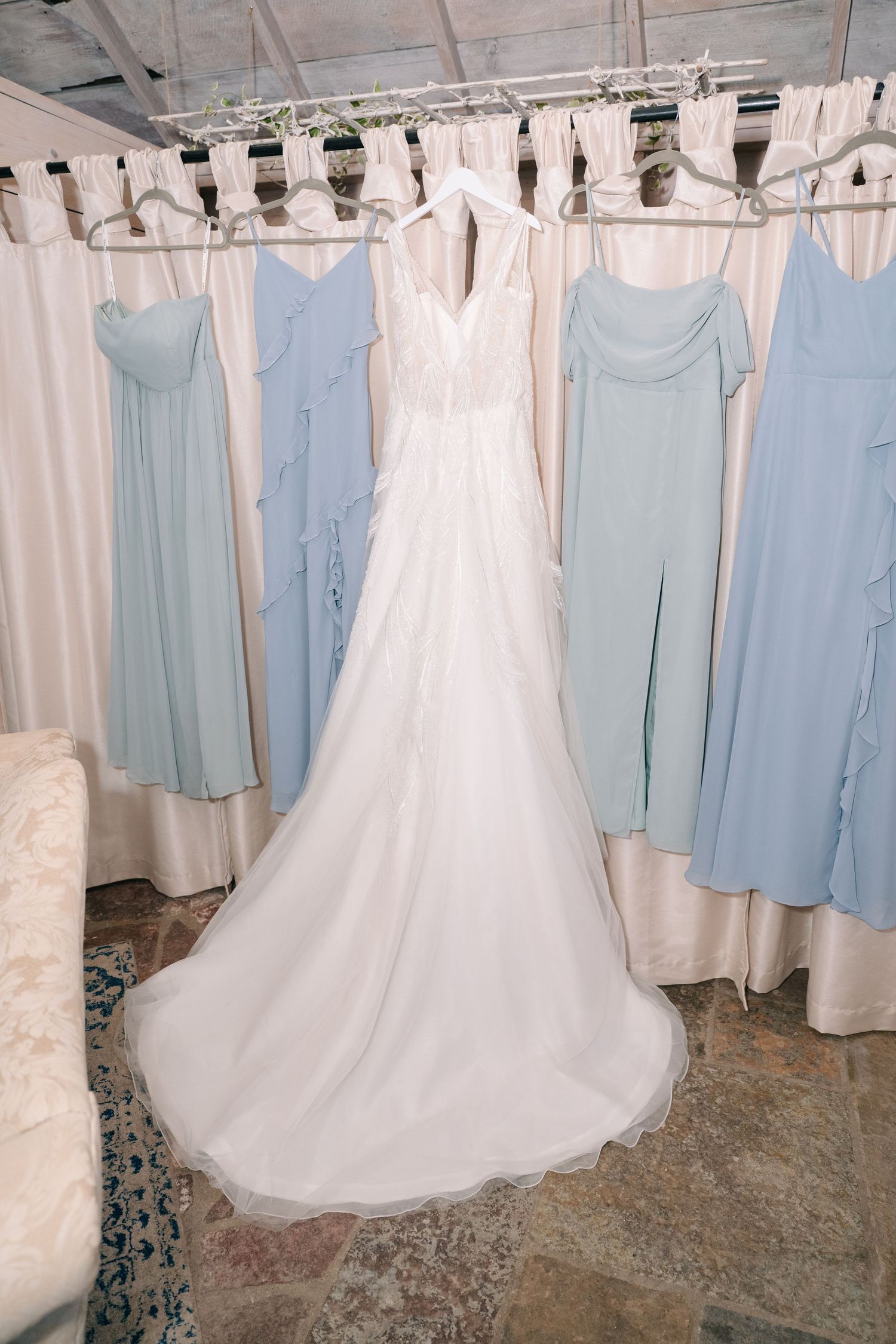 crooked willow weddings A white wedding gown displayed alongside light blue bridesmaid dresses on a rack.