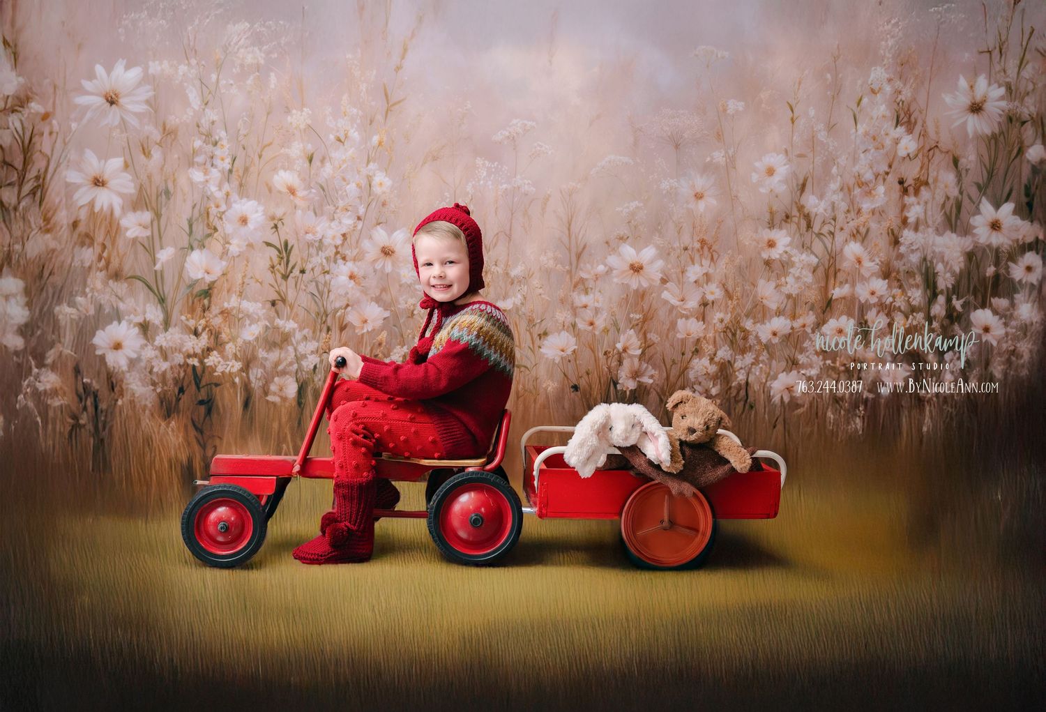 6 Year Old in a red knit outfit riding a toy tricycle with a wagon carrying stuffed animals against a floral backdrop. mother day photoshoot