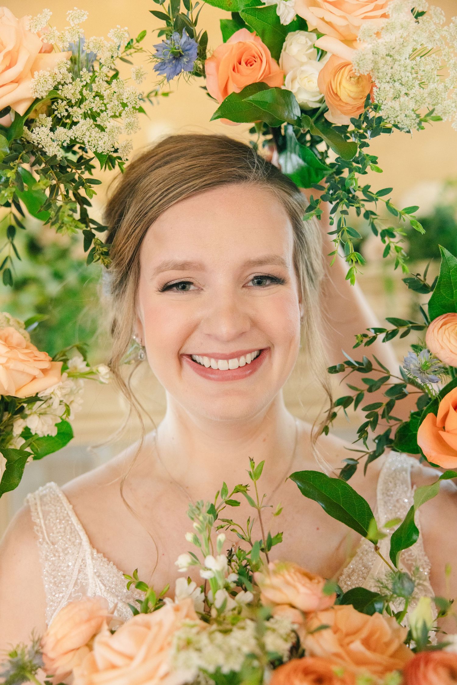 Smiling bride surrounded by peach roses and greenery bouquet on her wedding day.