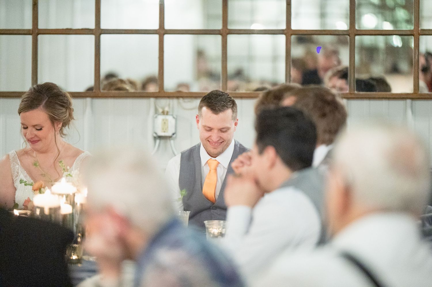 Bride and groom smiling at candlelit head table during wedding reception dinner.