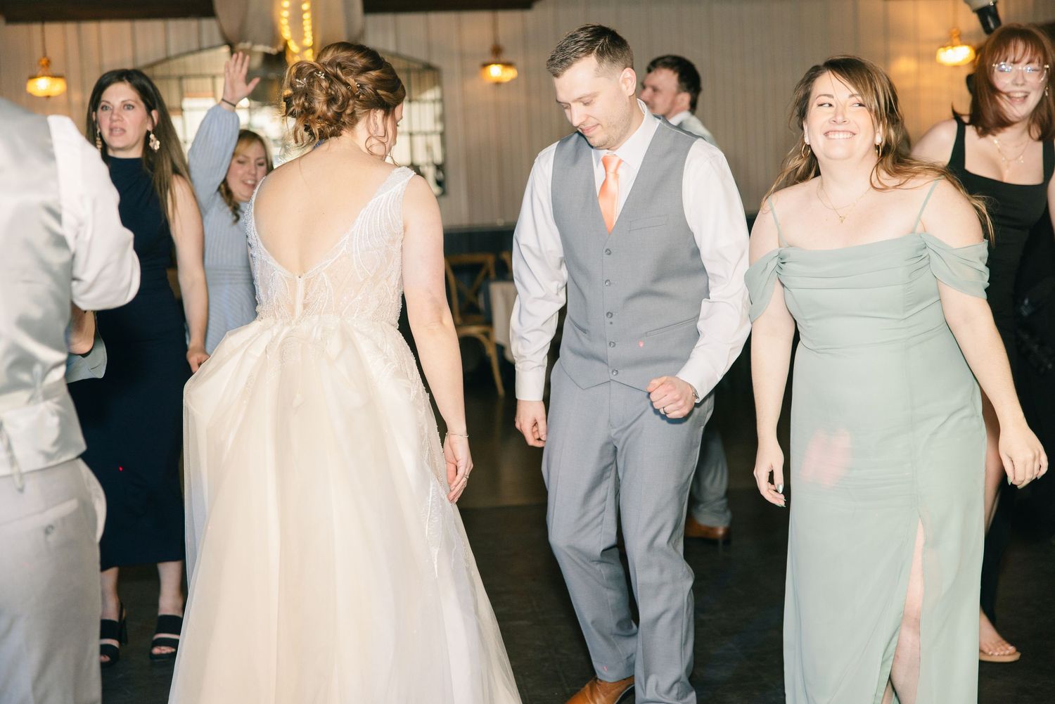 Bride and groom walk hand in hand on dance floor with wedding guests celebrating around them.